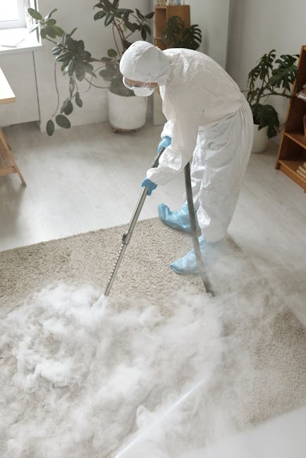 A person operating a vacuum cleaner on a wooden floor in a domestic setting, with the focus on the vacuum's nozzle and hose. The individual is wearing grey shorts, grey socks, and slippers, and is sta